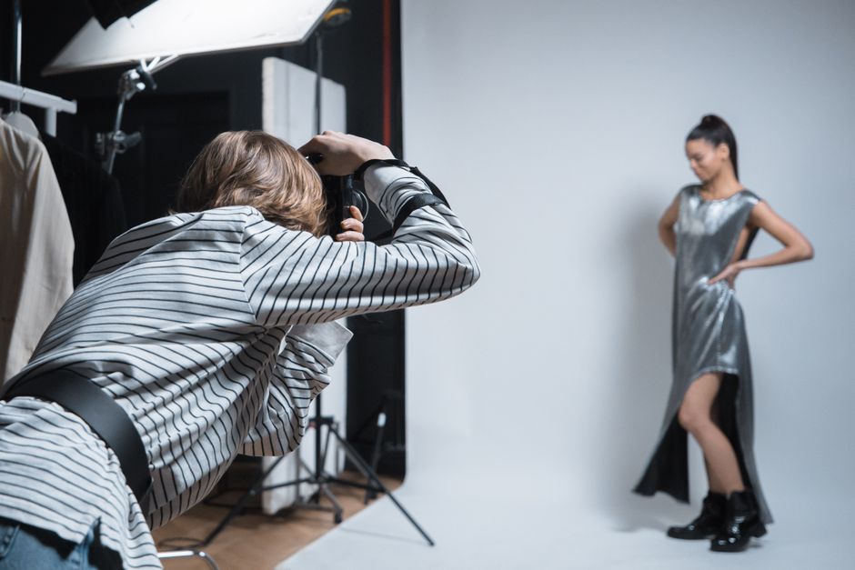Sessão de fotos profissional em estúdio com modelo feminina posando e fotógrafo capturando o momento.