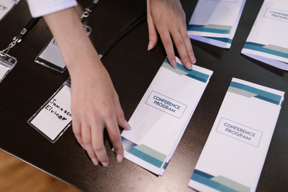 Pessoa organizando materiais para uma conferência, com pastas e crachás de identificação na mesa.