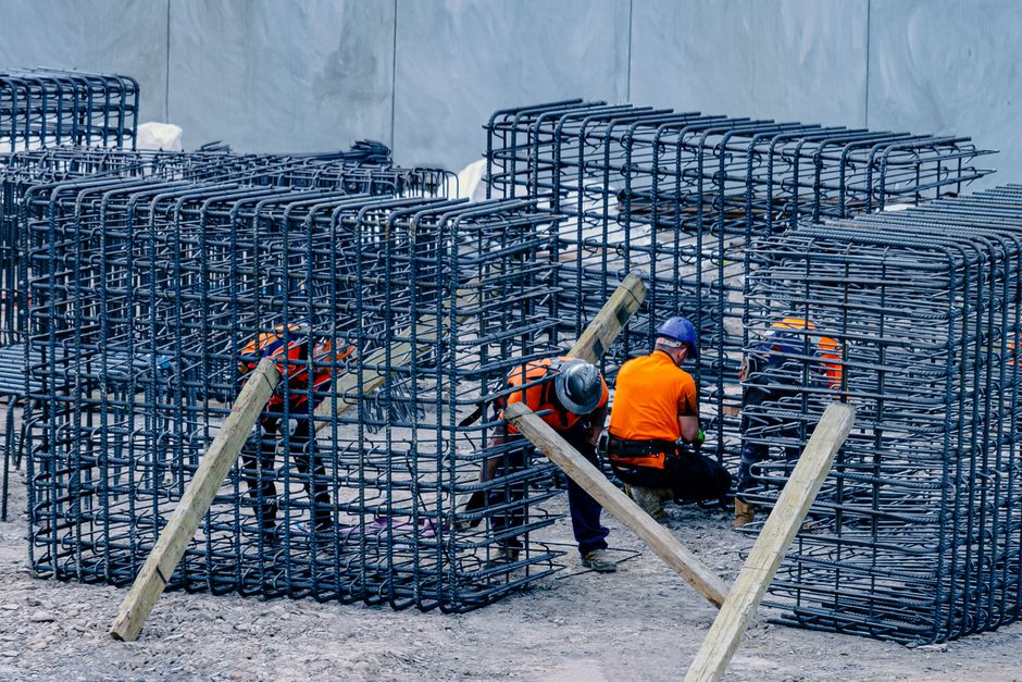 Imagem de trabalhadores em fase de construção, manipulando estruturas de aço reforçado em uma obra civil.