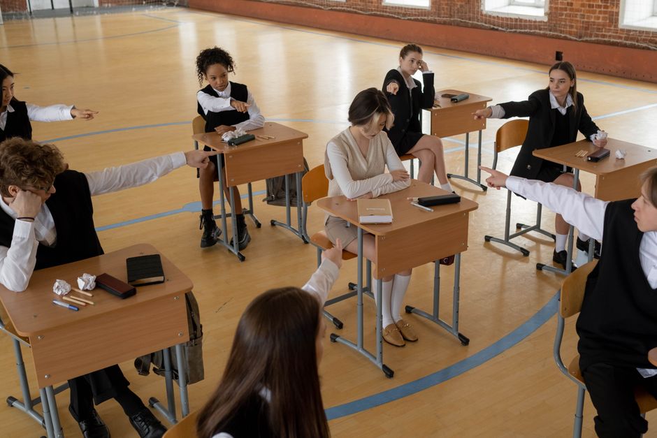Grupo de estudantes em sala de aula participando de atividade de discussão ou debate escolar, com professor mediando a conversa.