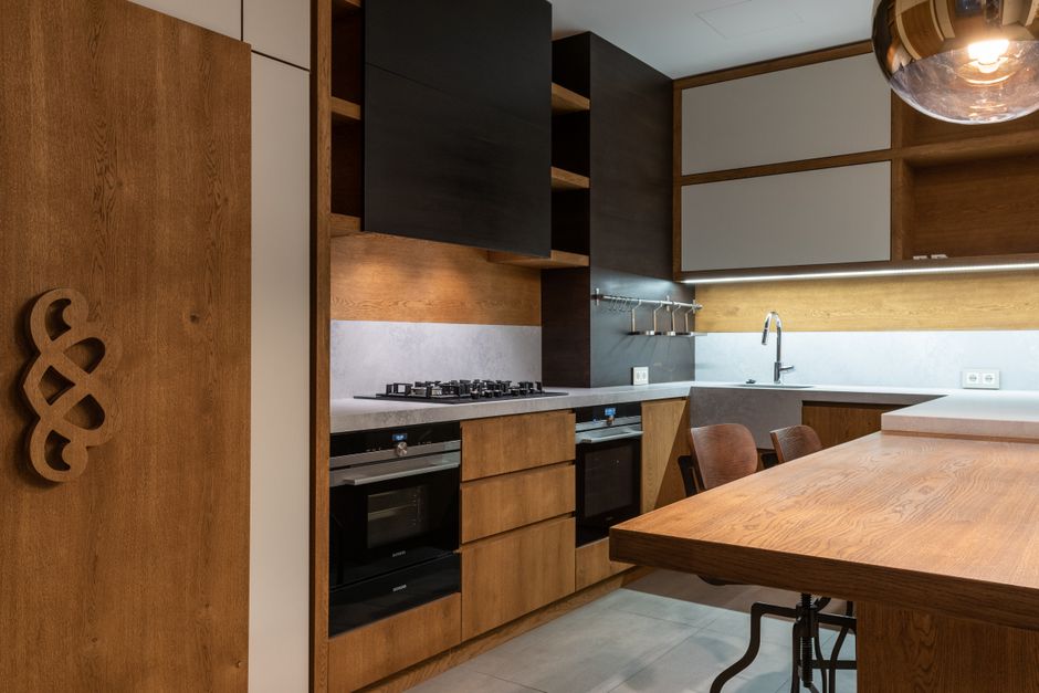 Cozinha moderna com acabamento em madeira, iluminação indireta e espaço para refeições e preparação de alimentos.