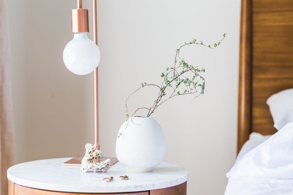 Imagem de uma mesinha de cabeceira com decoração minimalista ao lado de uma cama, destacando elementos de design de interiores com enfoque em ambientes de descanso e estilo de vida.