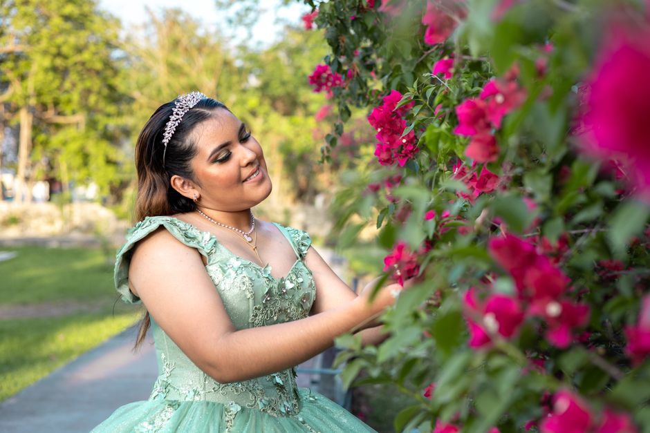 Mulher vestida de festa apreciando flores em um jardim, capturando um momento de tranquilidade e beleza natural.