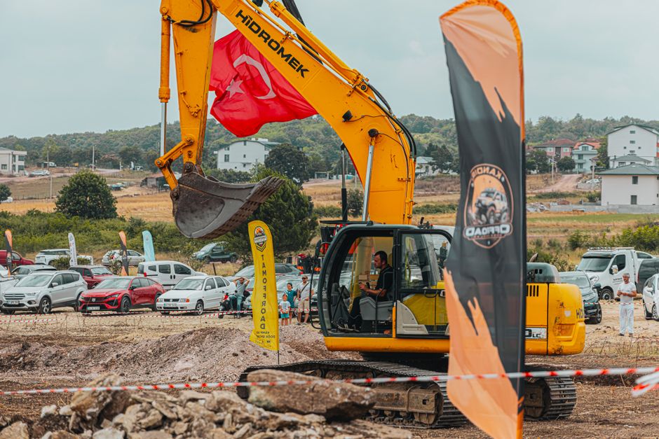 Maquinário de construção operando em projeto de urbanização com veículos de passeio ao fundo