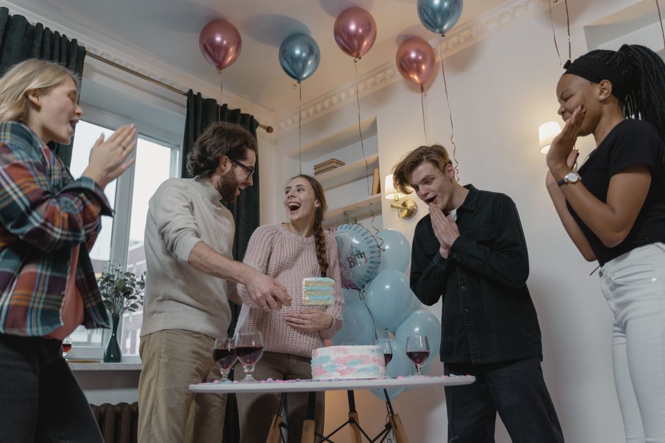 Grupo de amigos celebrando um aniversário em uma festa decorada com balões e um bolo, demonstrando alegria e confraternização.