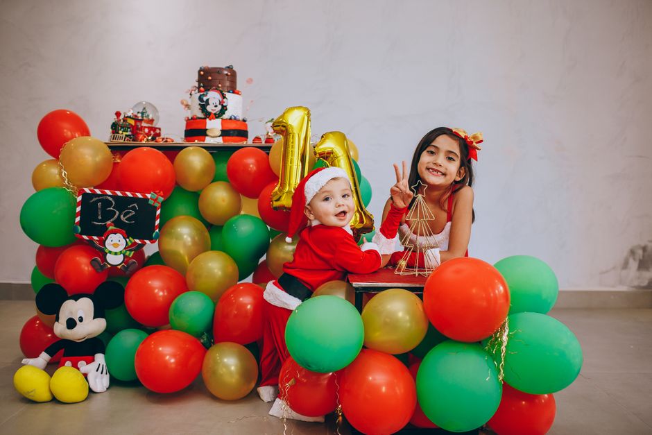 Crianças comemorando o Natal com decoração temática, balões coloridos e aniversário em um ambiente festivo.
