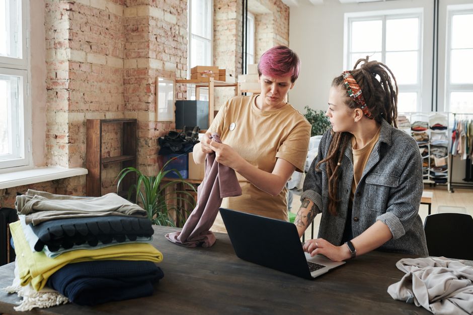Duas mulheres trabalhando juntas em um ambiente de escritório com foco em organização e planejamento de produtos de vestuário.