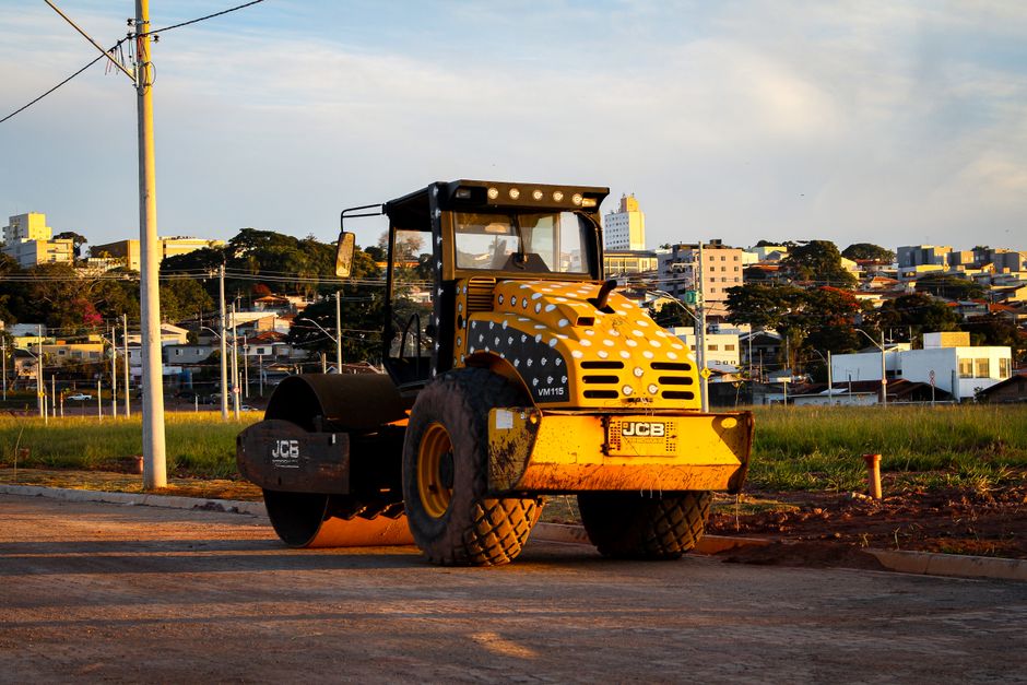 Foto de um pavimentador de ruas em um projeto de infraestrutura urbana ao pôr do sol, com vista para a cidade ao fundo.