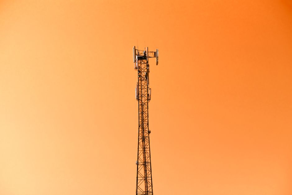 Antena de telecomunicações em um céu laranja, simbolizando conectividade e tecnologia moderna.