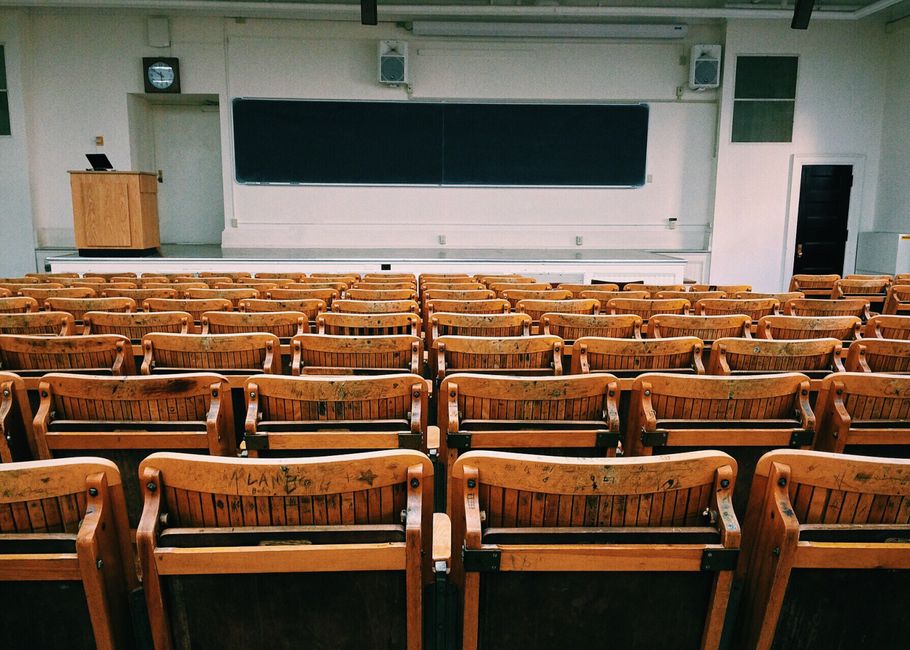 Sala de aula vazia, com assentos de madeira e quadro-negro, representando educação e ensino presencial.