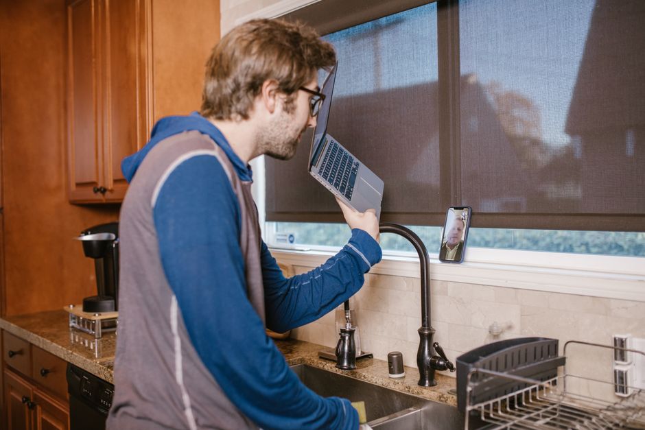 Homem realizando uma videochamada de trabalho na cozinha, ilustrando o ambiente de home office e a conexão digital.