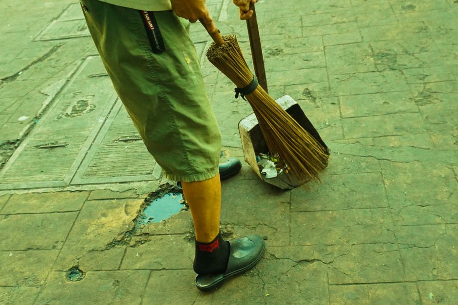 Pessoa varrendo calçada com cuidado em ambiente urbano, destacando a importância da higiene pública e manutenção de espaços urbanos.