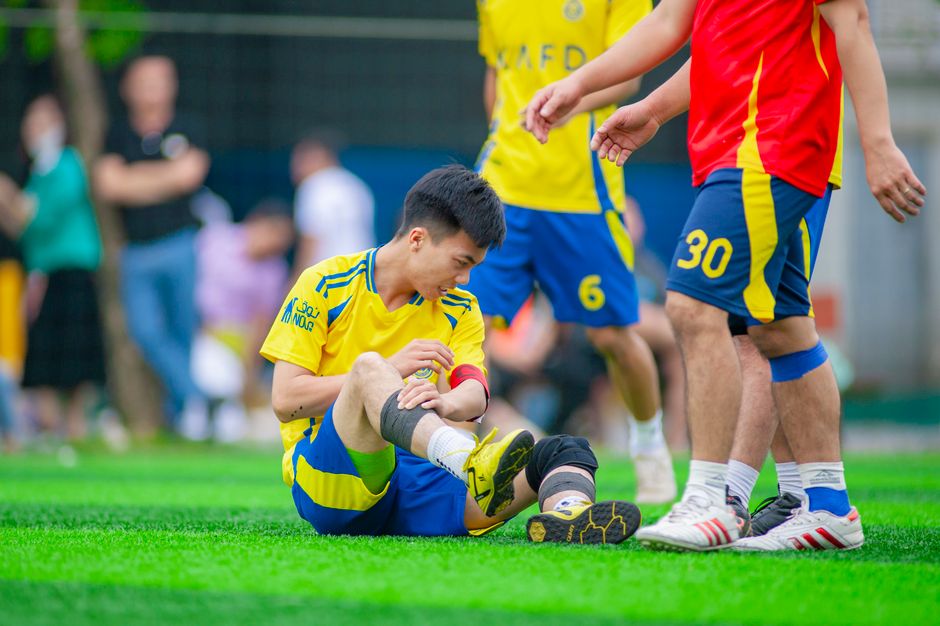 Jogador de futebol ferido sendo atendido por companheiros em campo durante uma partida escolar ou recreativa.