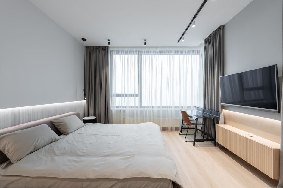 Imagem de um quarto moderno e minimalista com grandes janelas, iluminação suave e decoração clean, ideal para um artigo sobre design de interiores ou hospedagem de luxo.