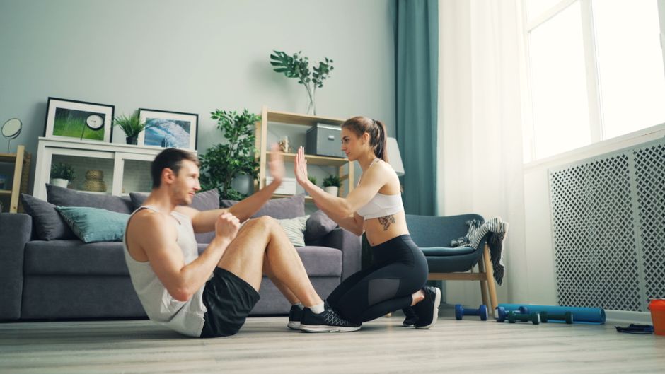 Imagem de um casal praticando exercícios físicos em casa, demonstrando incentivo à rotina de treinos e bem-estar no ambiente doméstico.