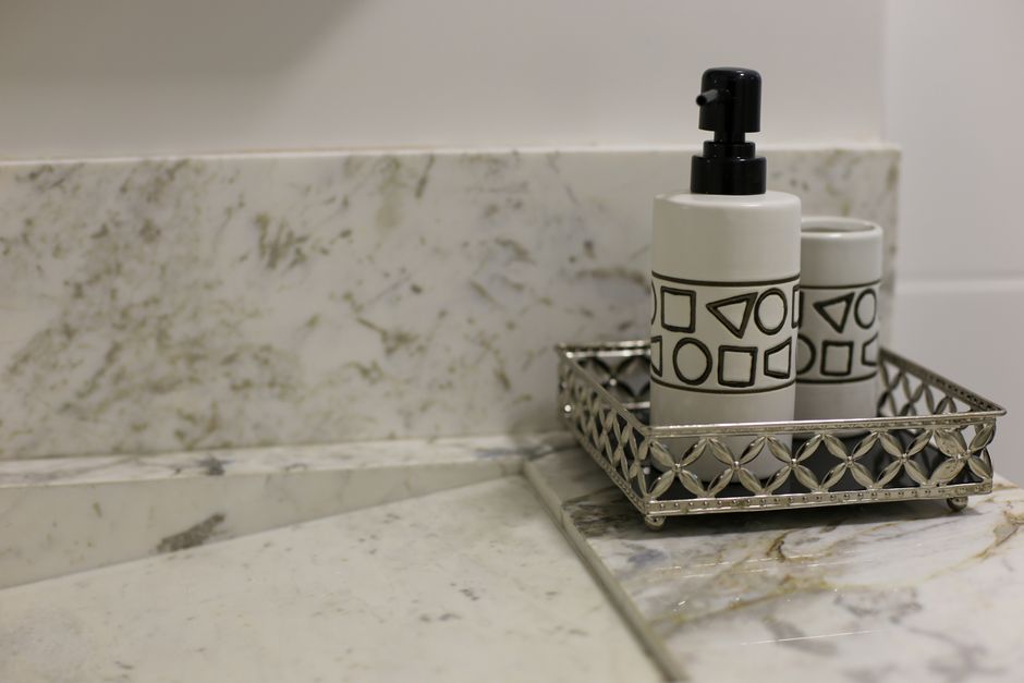 Imagem de produtos de higiene e decoração de banheiro com frascos de sabonete ou loção em uma bandeja metálica sobre uma bancada de mármore.
