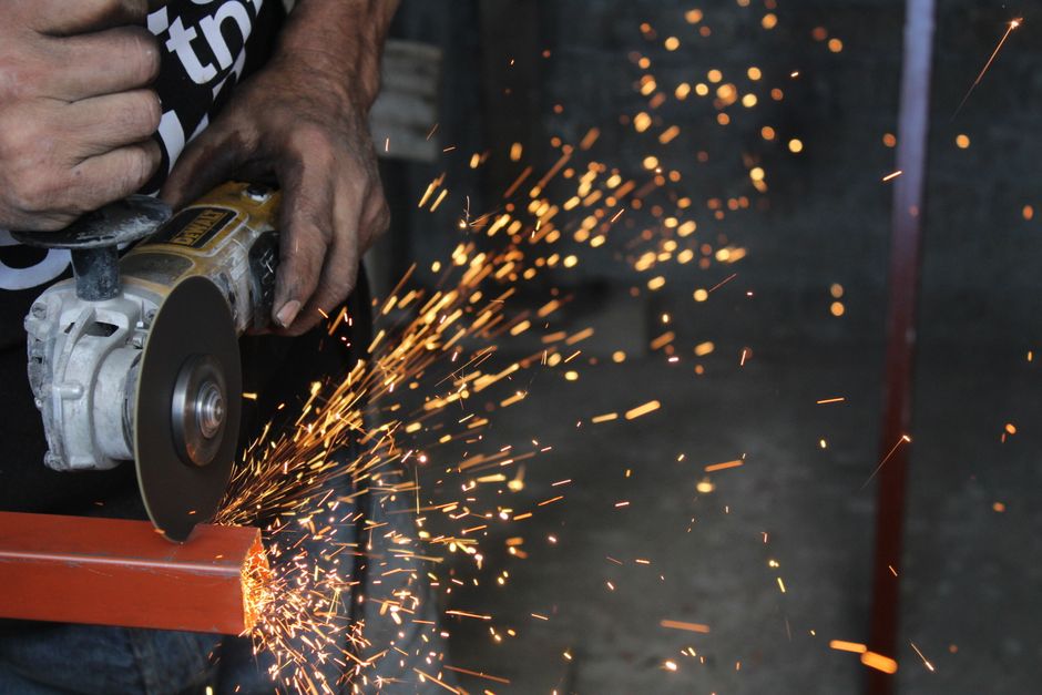 Pessoa utilizando uma serra de bancada para cortar uma peça de metal no ambiente de uma oficina ou garagem.