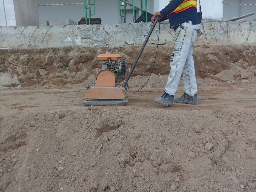 Profissional de construção civil utilizando uma régua mecânica para nivelamento de terreno em uma obra em andamento.