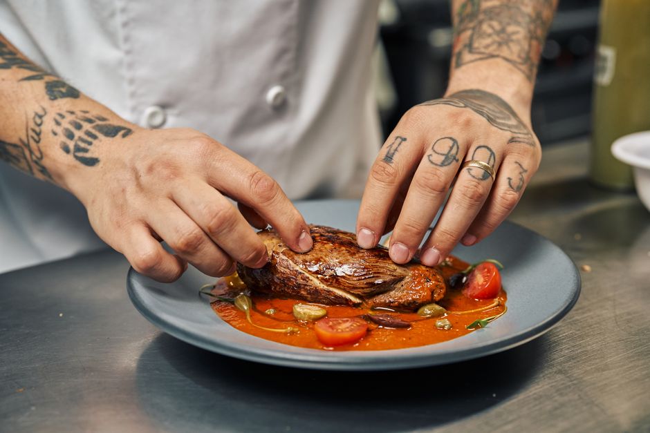 Chef preparando um prato de comida sofisticado em uma cozinha profissional, destacando a atenção aos detalhes na gastronomia.