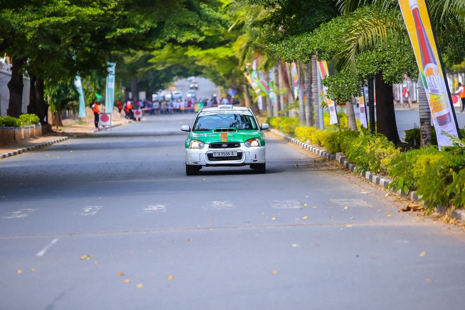 Carro de rally trafegando por uma rua arborizada, celebrando eventos automobilísticos ao ar livre.