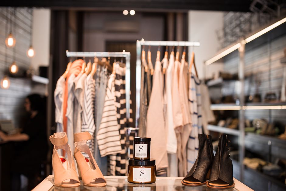 Imagem de loja de roupas e acessórios femininos com destaque para calçados e vestuário no ambiente de um pequeno comércio ou boutique.