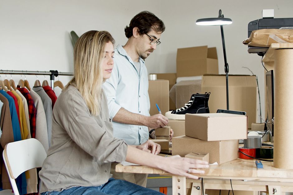 Dois empreendedores trabalhando na montagem de produtos e gerenciando seu negócio em um ambiente de loja ou atelier de moda.