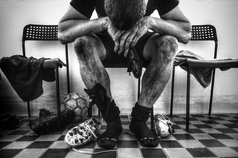 Imagem de um atleta cansado após partida de futsal, sentado em um banco de vestiário, refletindo sobre o esforço físico.