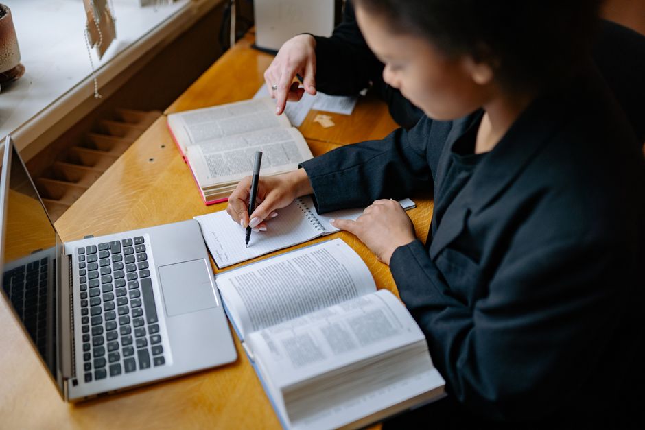Pessoas estudando e analisando materiais acadêmicos e digitais em um ambiente de estudo ou trabalho, com foco em pesquisa e preparação.