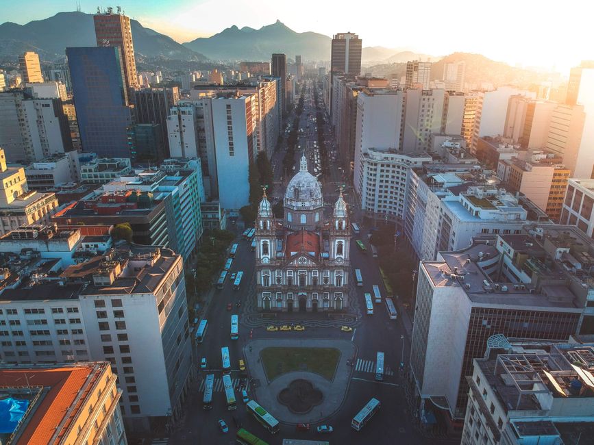 Vista aérea de uma cidade movimentada ao pôr do sol, com destaque para uma igreja histórica no centro, refletindo a combinação entre patrimônio cultural e vida urbana moderna.