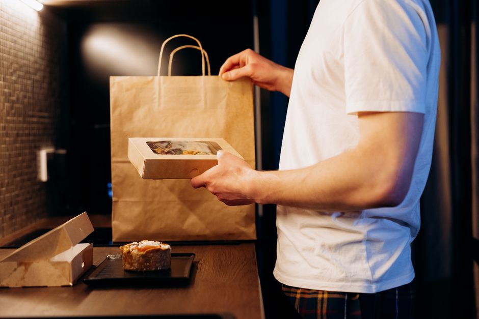 Pessoa recebendo uma caixa de comida para entrega em um ambiente interno, destacando o tema de delivery e gastronomia.