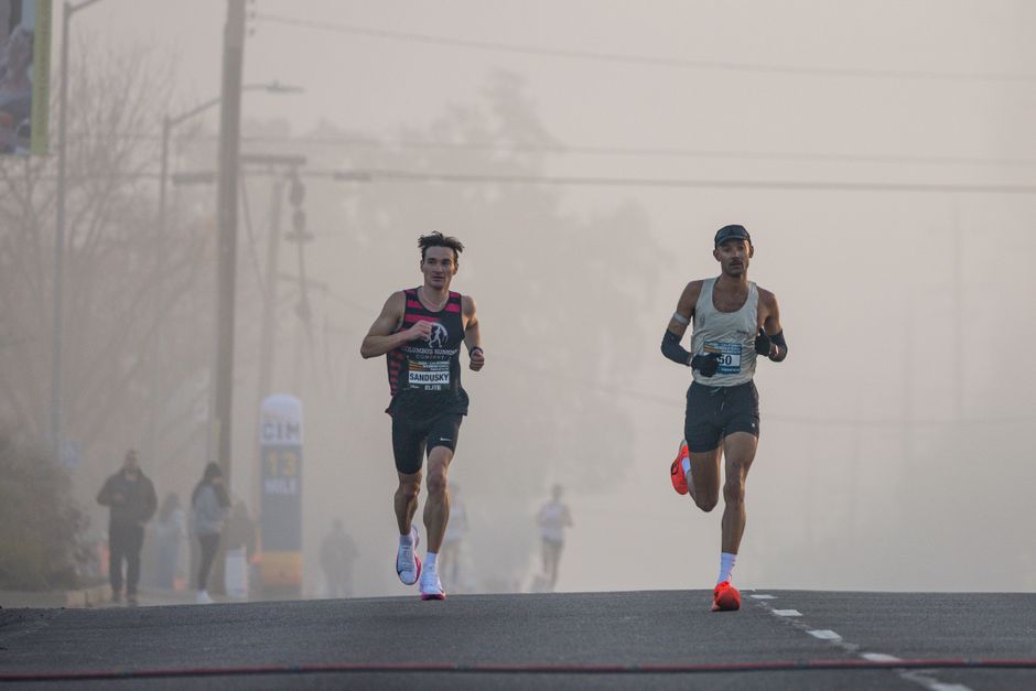 Dois corredores participam de uma prova de corrida em clima de manhã com névoa, transmitindo foco e resistência esportiva.