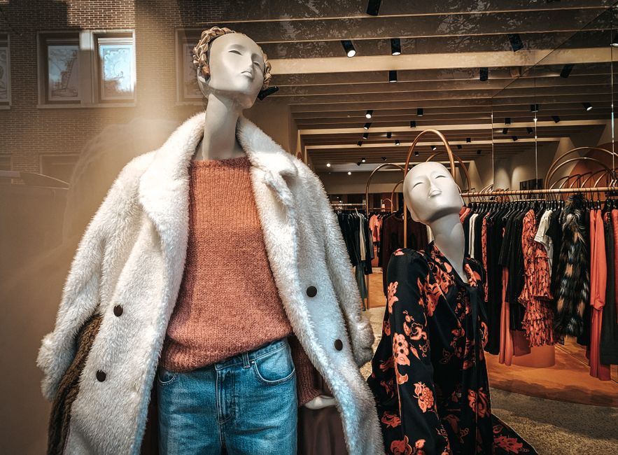Manquês de roupas femininas exibindo tendências de moda em uma vitrine de loja de roupas de alto padrão.