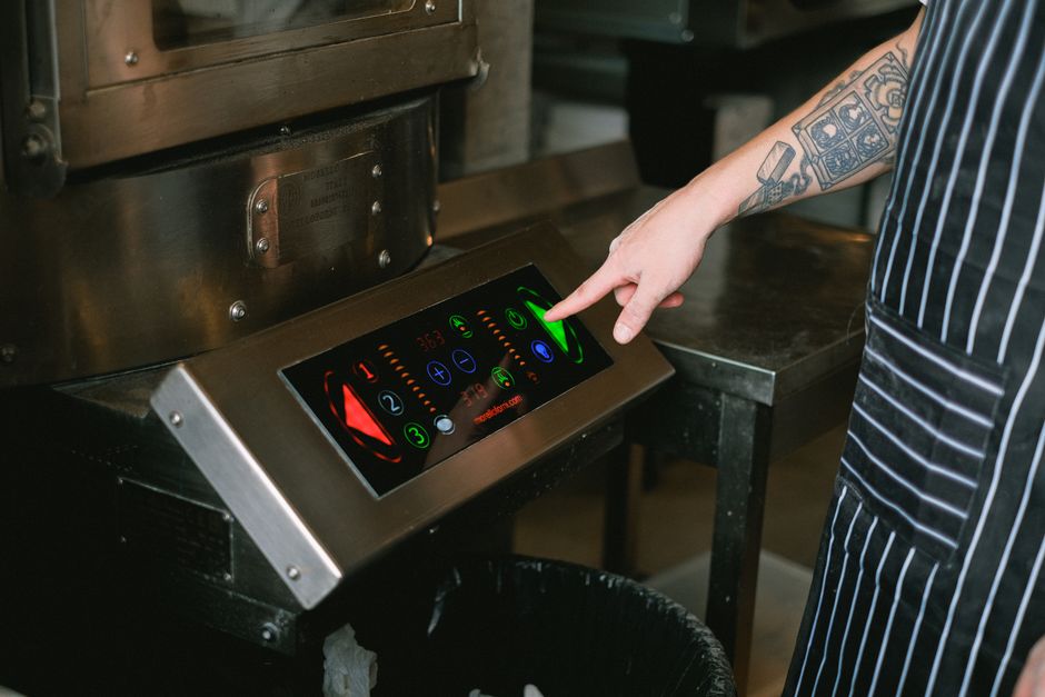 Pessoa operando um painel digital de controle em uma cozinha profissional, destacando a tecnologia na gastronomia.