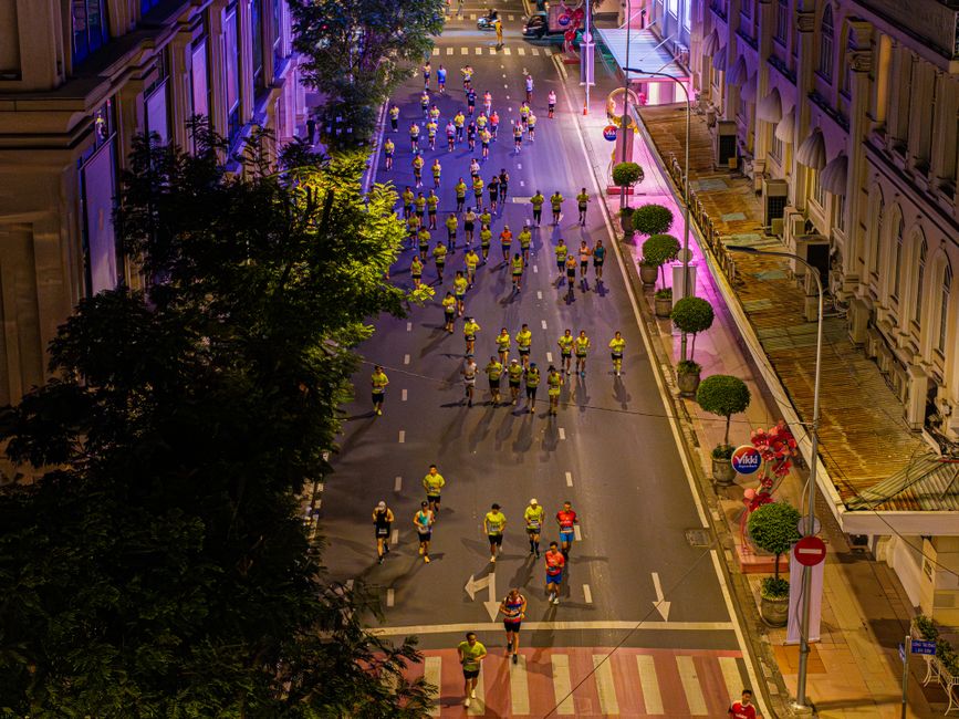 Corredores participando de uma corrida de rua noturna pela cidade, com ruas fechadas ao trânsito e iluminação urbana vibrante.