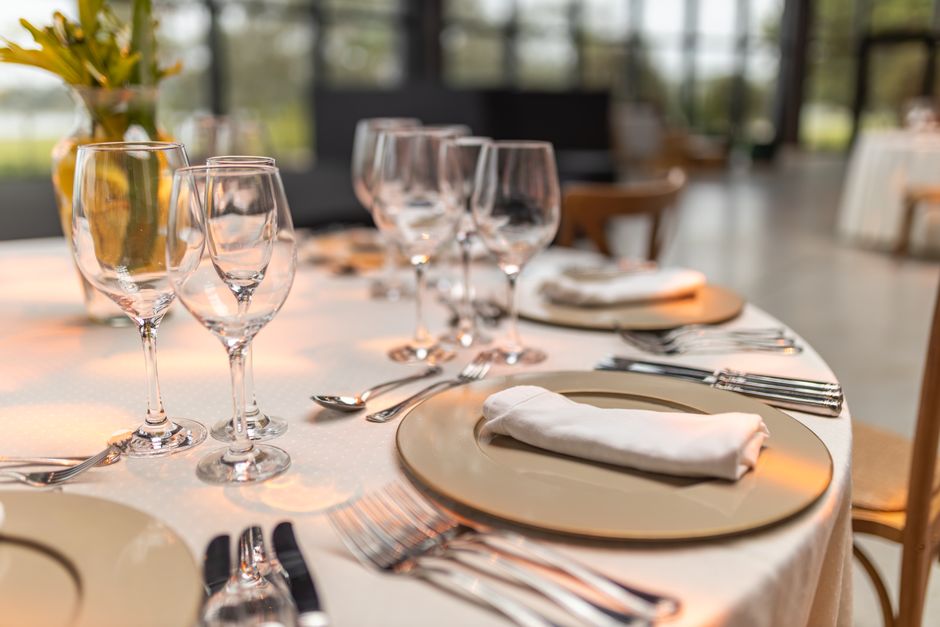 Mesa elegantemente preparada para um jantar sofisticado, com taças de vinho, pratos e talheres dispostos de forma organizada.