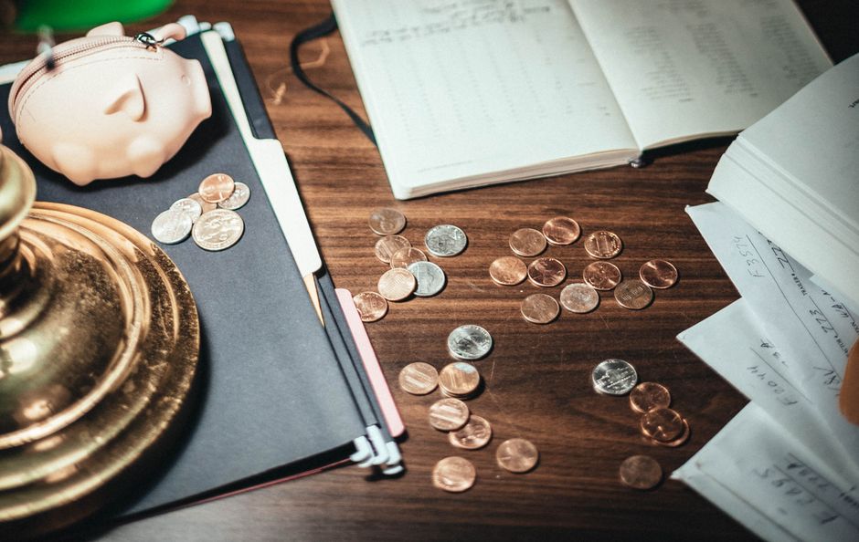 Imagem de uma mesa de escritório com notas, moedas e materiais de trabalho, representando gestão financeira e controle de despesas.