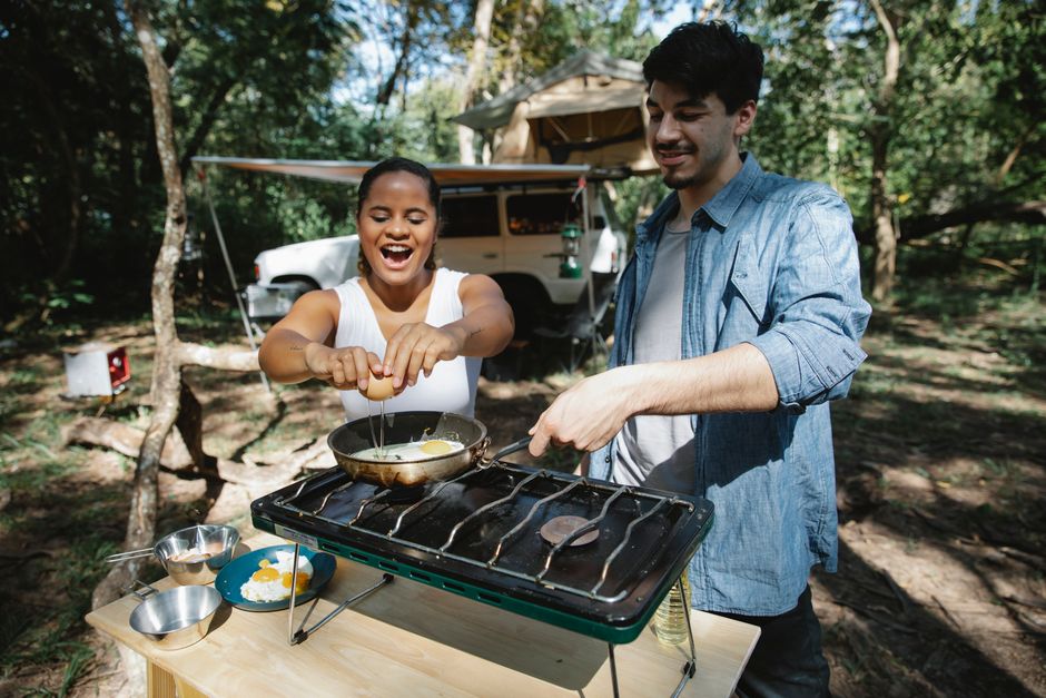 Casal feliz preparando refeição ao ar livre durante camping em meio à natureza
