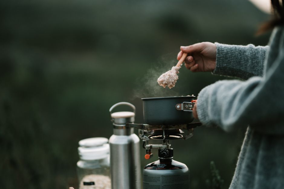 Pessoa cozinhando ao ar livre com uma panela portátil, em contato com a natureza, ideal para um artigo sobre culinária sustentável ao ar livre.