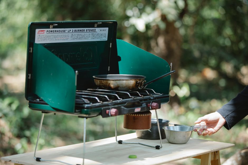 Imagem de um fogão portátil ao ar livre sendo utilizado para cozinhar em ambiente natural, destacando o conceito de culinária ao ar livre ou camping.