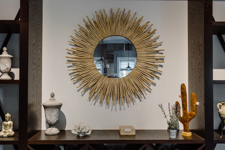 Espelho decorativo em formato de sol, em um ambiente que combina elementos de decoração rústica e moderna, refletindo a sala ao fundo.