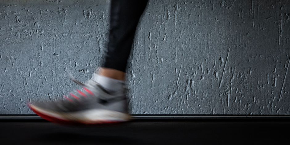 Pessoa caminhando rapidamente, simbolizando movimento e progresso, em um ambiente interno com parede de texture rústica.
