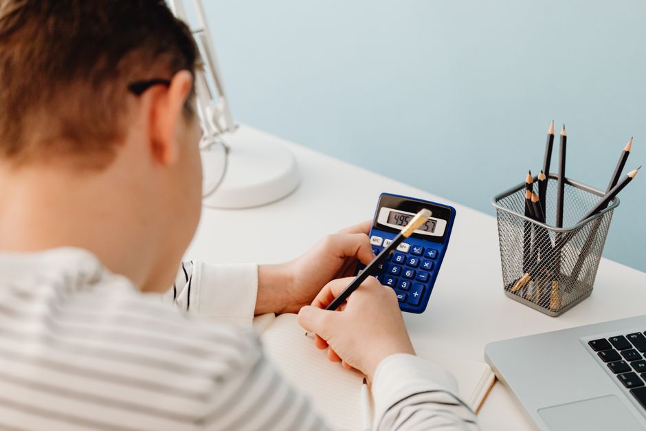 Pessoa analisando planilha financeira com calculadora em ambiente de escritório, focada em gestão de finanças pessoais ou empresariais.