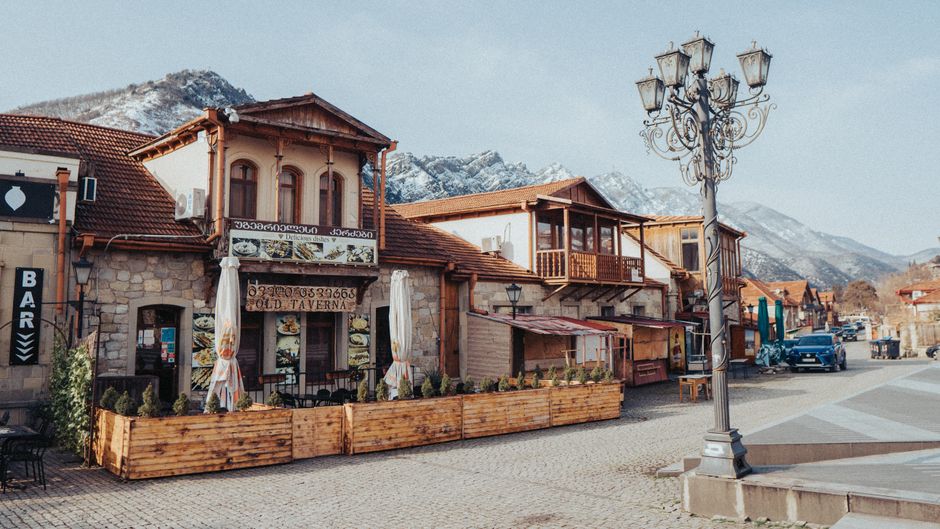 Vista de uma rua de vila com arquitetura tradicional em meio a uma paisagem montanhosa com nevascas, refletindo o charme de uma cidade turística de inverno.