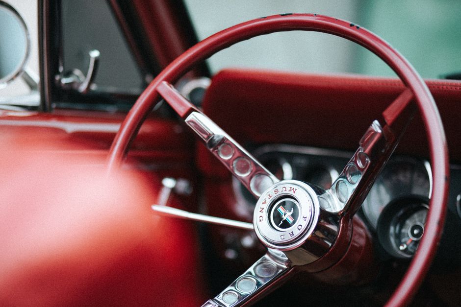 Imagem de um interior clássico de carro vintage com destaque para o volante vermelho e detalhes em chrome, transmitindo nostalgia e estilo retrô.