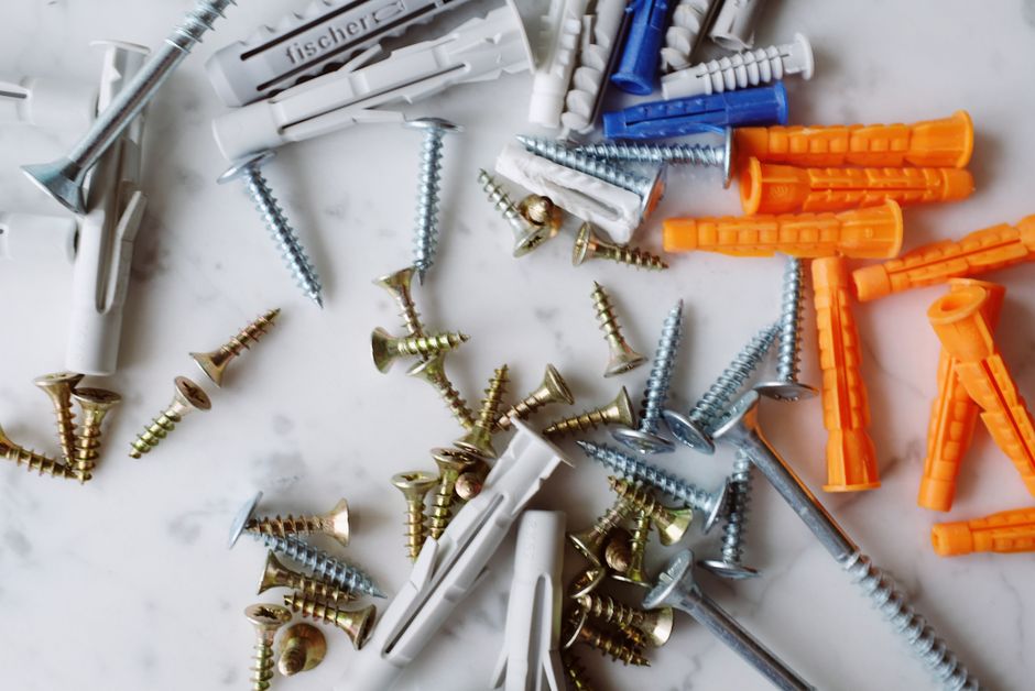 Imagem de várias presilhas, parafusos e bucha de parede, representando a organização de materiais de construção ou reforma.