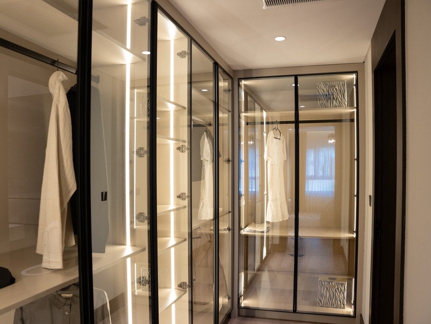 Closet sofisticado com portas de vidro e iluminação embutida, ideal para organização de roupas e acessórios em ambientes residenciais modernos.