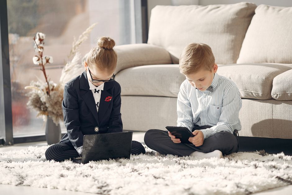 Crianças utilizando dispositivos eletrônicos em ambiente doméstico, refletindo o tema de tecnologia e educação infantil.