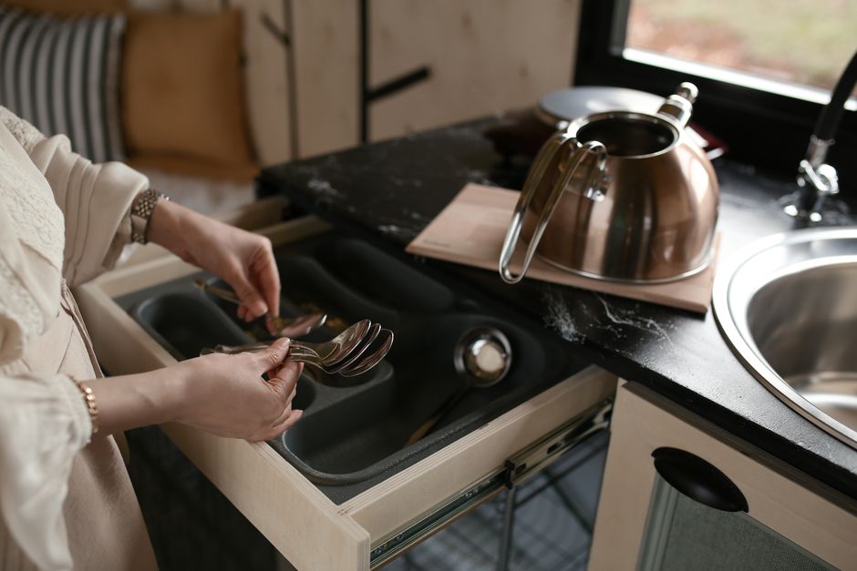 Pessoa organizando talheres em uma gaveta de cozinha, destacando a rotina doméstica e organização do ambiente.