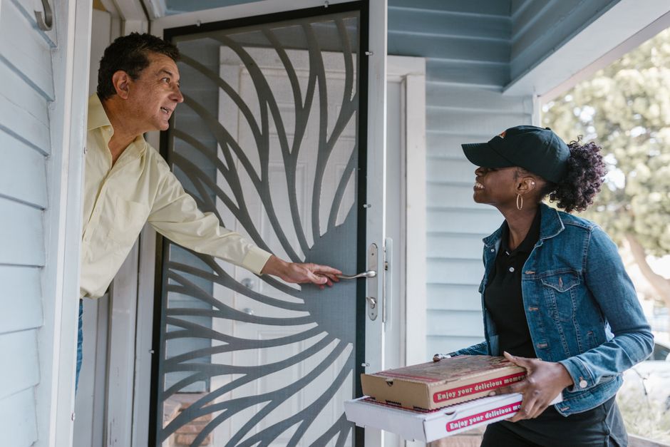 Uma entrega de pizza sendo feita na porta de uma casa, simbolizando serviços de delivery ou contato delivery com clientes.