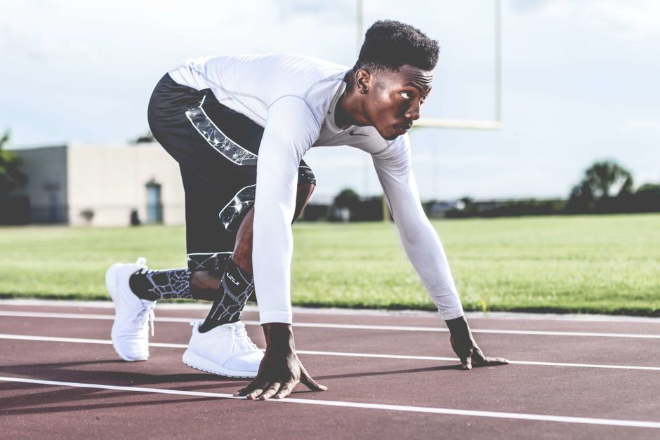 Atleta em posição de partida em uma pista de corrida, preparado para uma prova de atletismo.